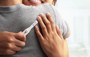 First Signs of Pregnancy: woman hugging partner while holding positive pregnancy test