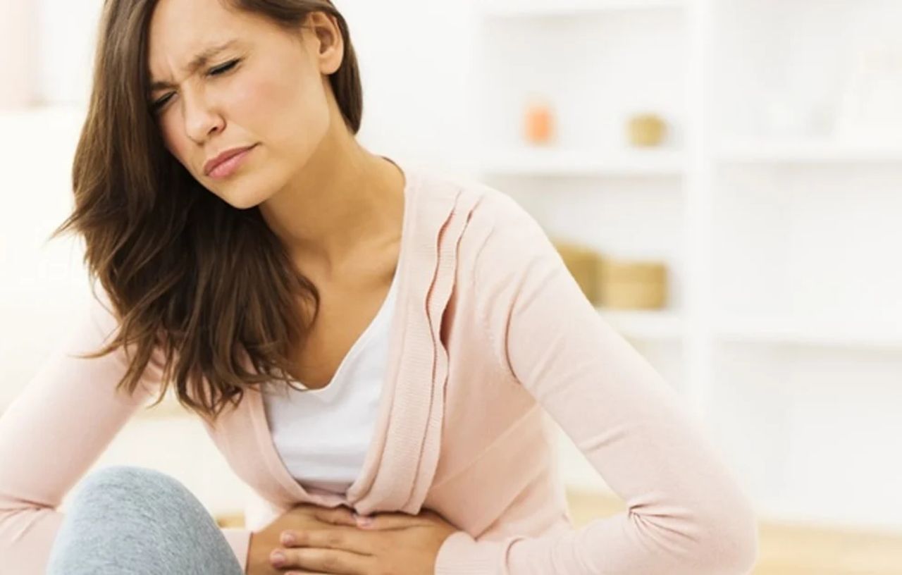 First Signs of Pregnancy: woman with abdominal discomfort holding her stomach, showing early pregnancy symptoms.