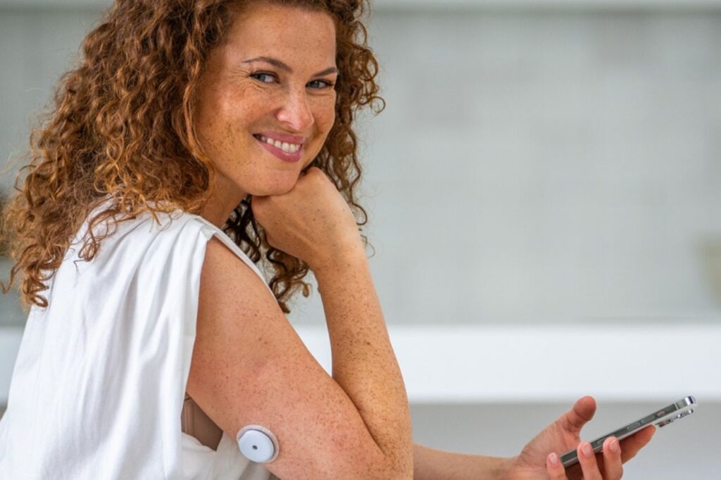 Woman using a glucose sensor on her arm and holding a smartphone with the mySugr app, symbolizing technology and well-being in diabetes management.