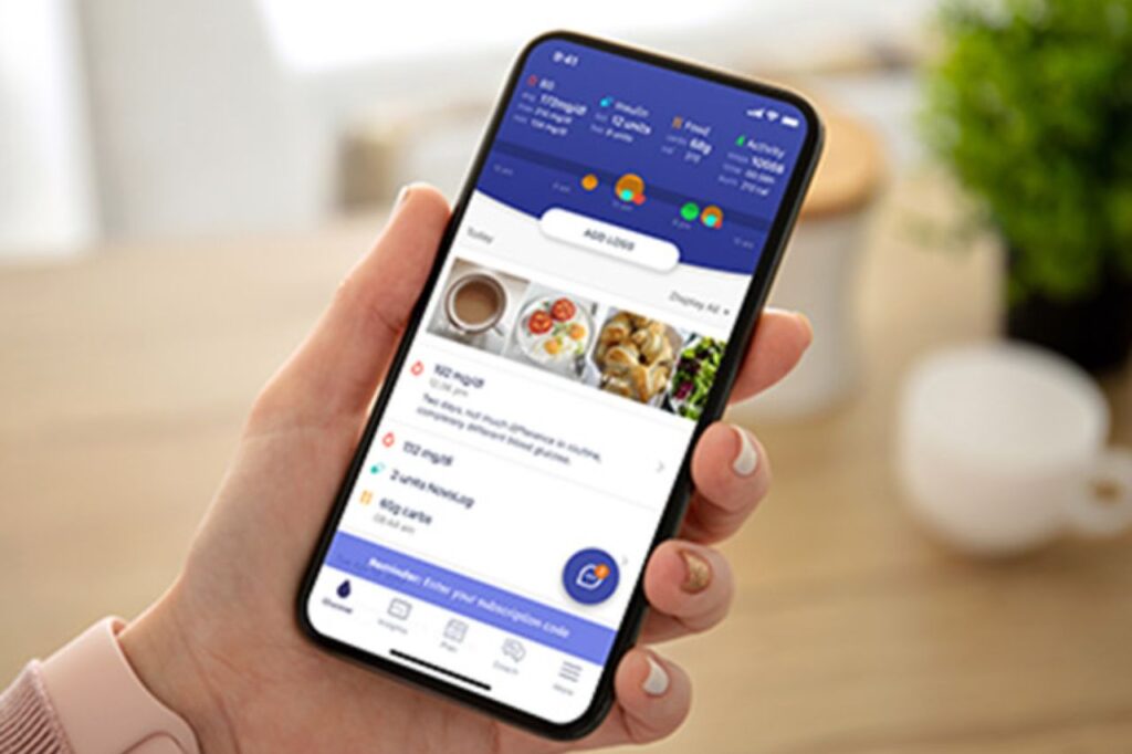 A person holding a smartphone with the Glucose Buddy app open, displaying meal logs and glucose levels in a clear and intuitive interface.